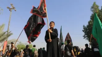 پسر نوجوانی که در میان زوار ایستاده و پرچم گردانی می کند